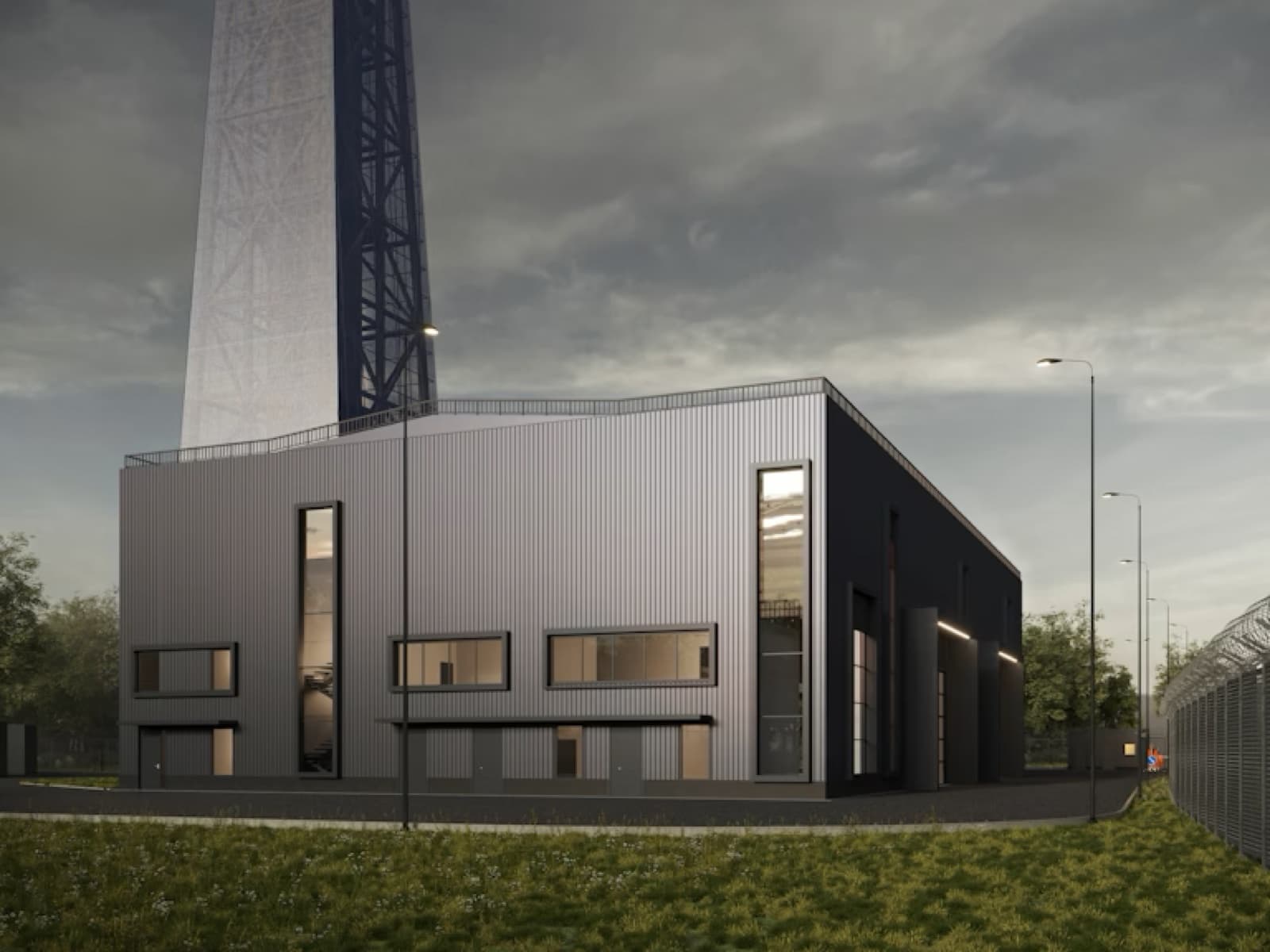 A metal-clad industrial plant beneath a lattice tower at dusk