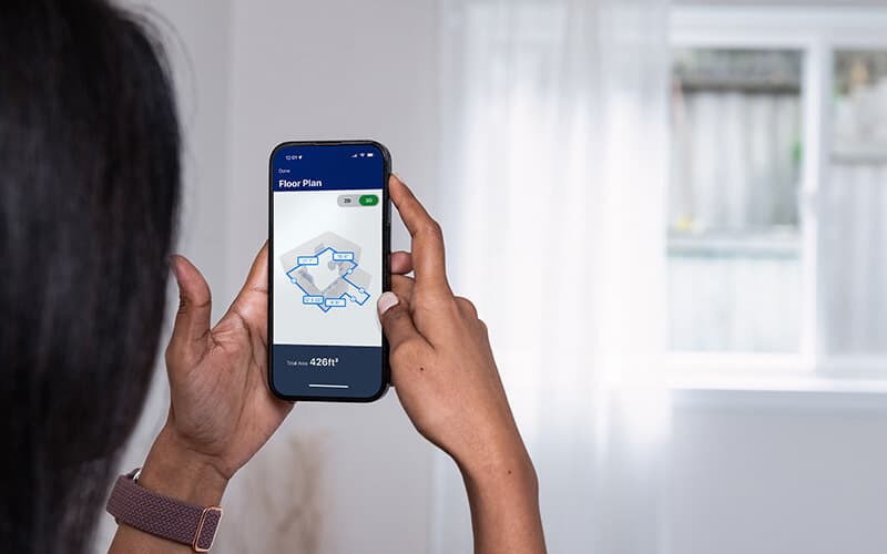 Hands holding a phone that displays a measured plan of the room it is pointed at.