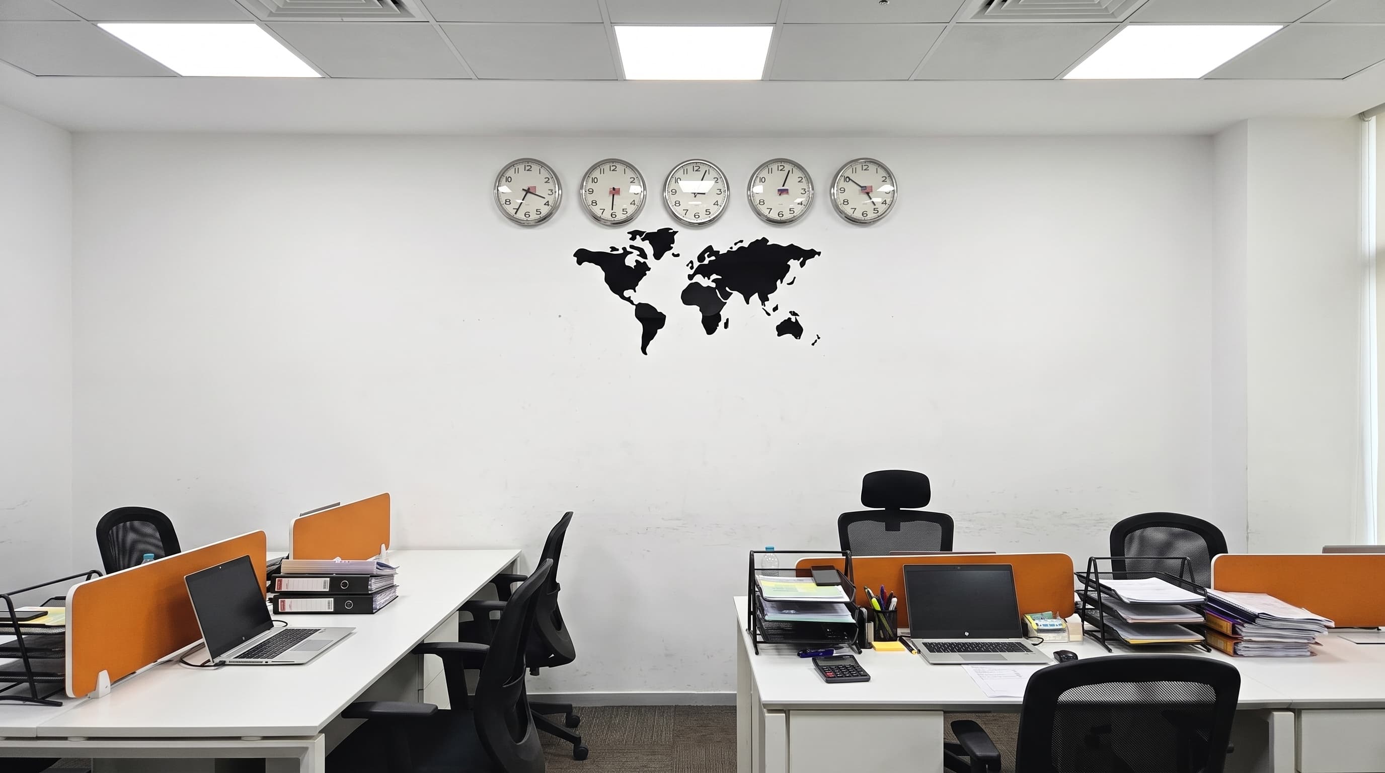 The MHBC open-plan floor: desks with orange dividers under a row of world-time clocks and a world map.