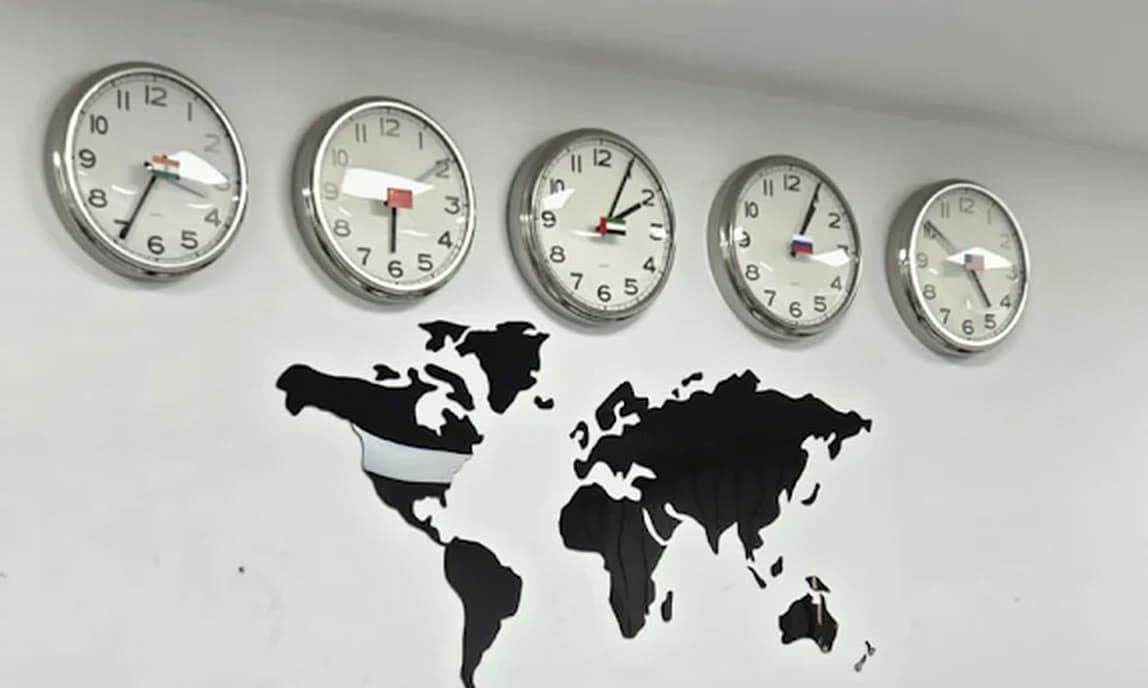 A row of clocks set to several time zones above a world map on the MHBC office wall.